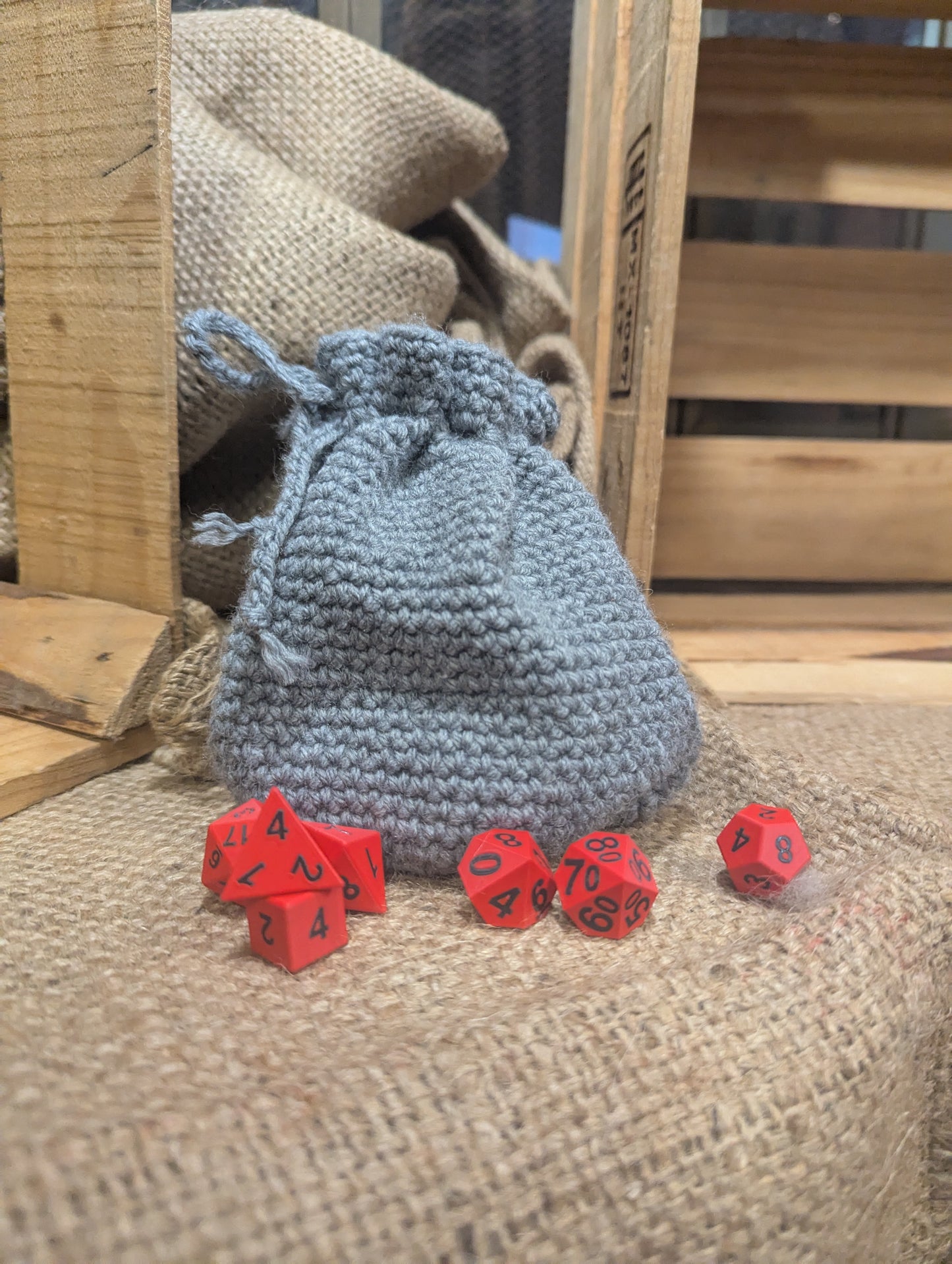 Gray crochet dice bag with red dice on a wooden surface