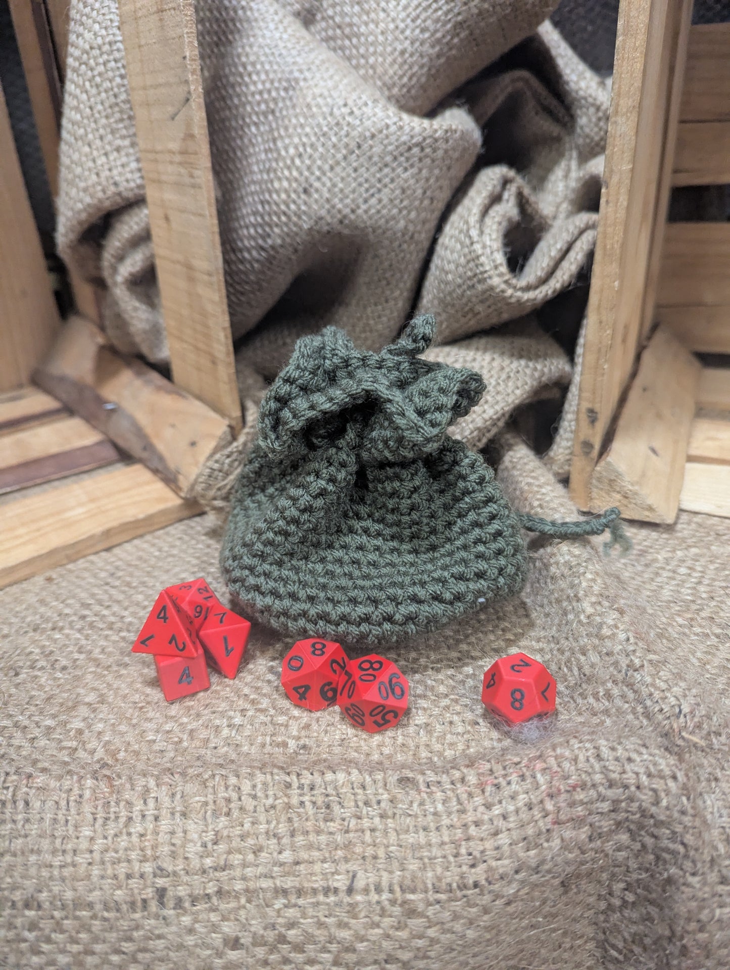 Crocheted green dice bag with red dice on a rustic wooden and fabric background