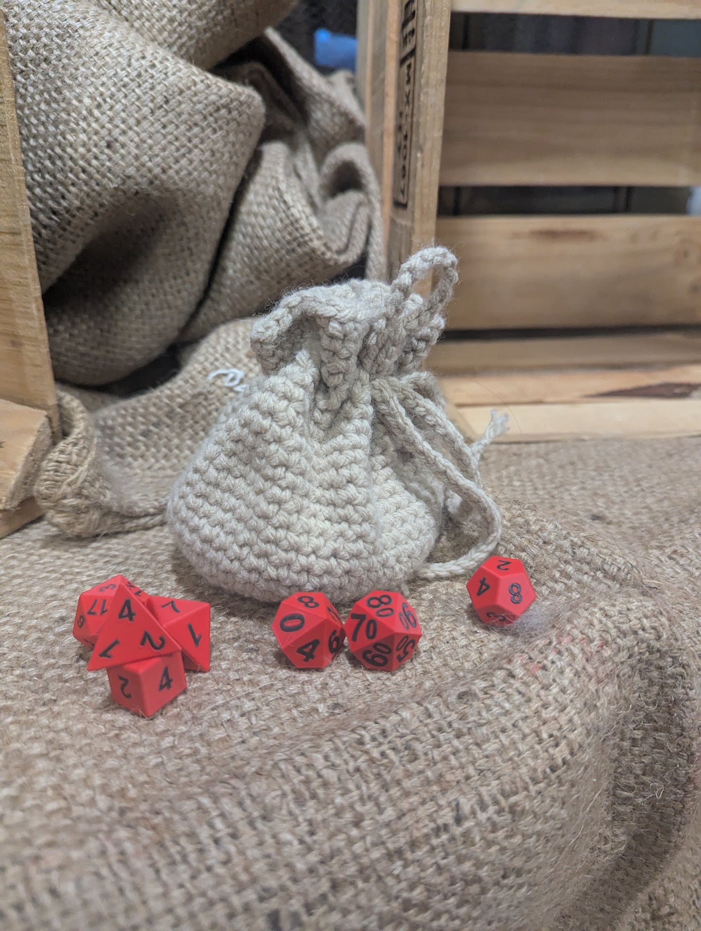 Red dice with black numbers on a textured surface next to a cream drawstring bag.