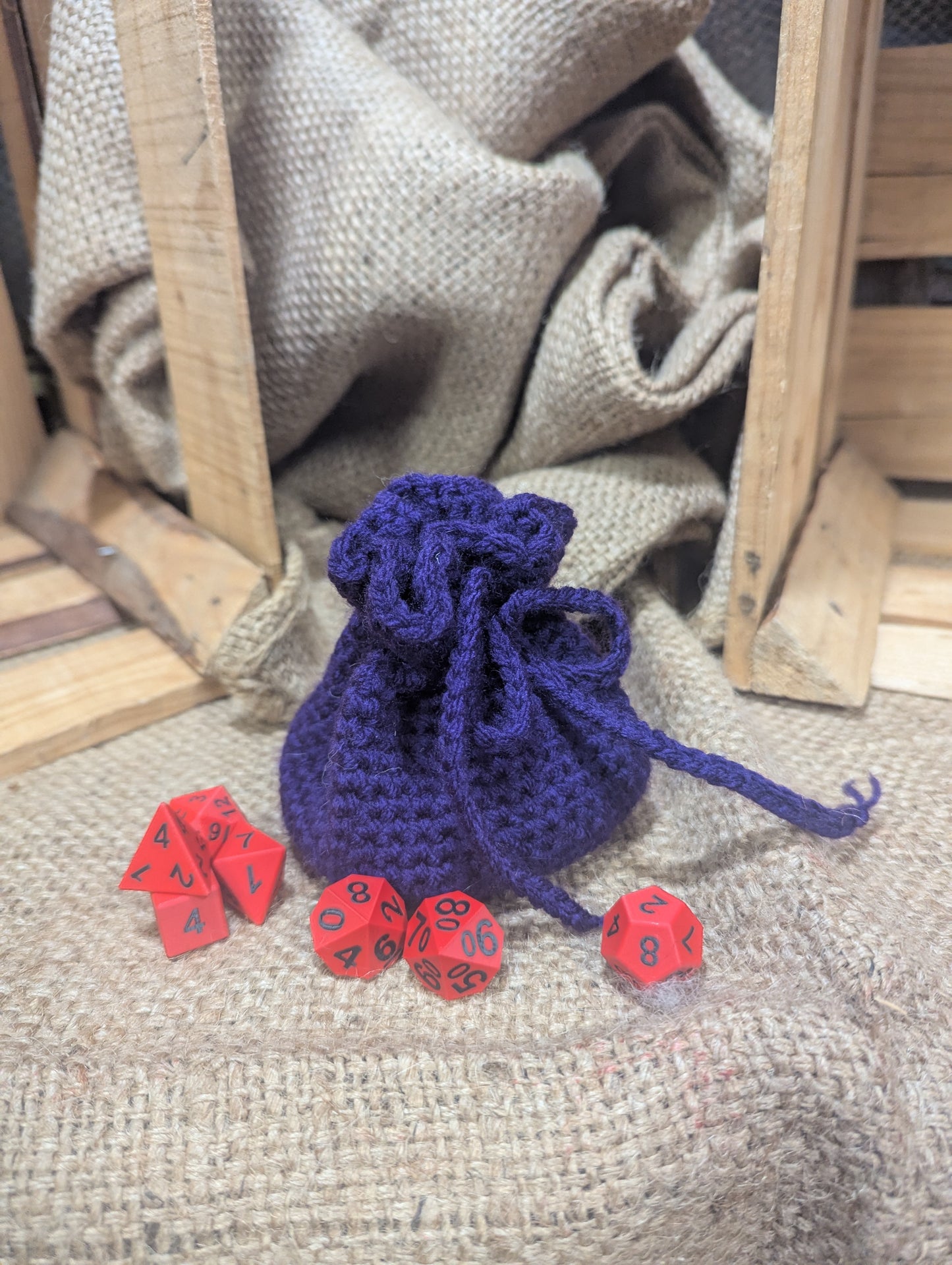 purple crochet dice bag with red dice on a rustic wooden surface