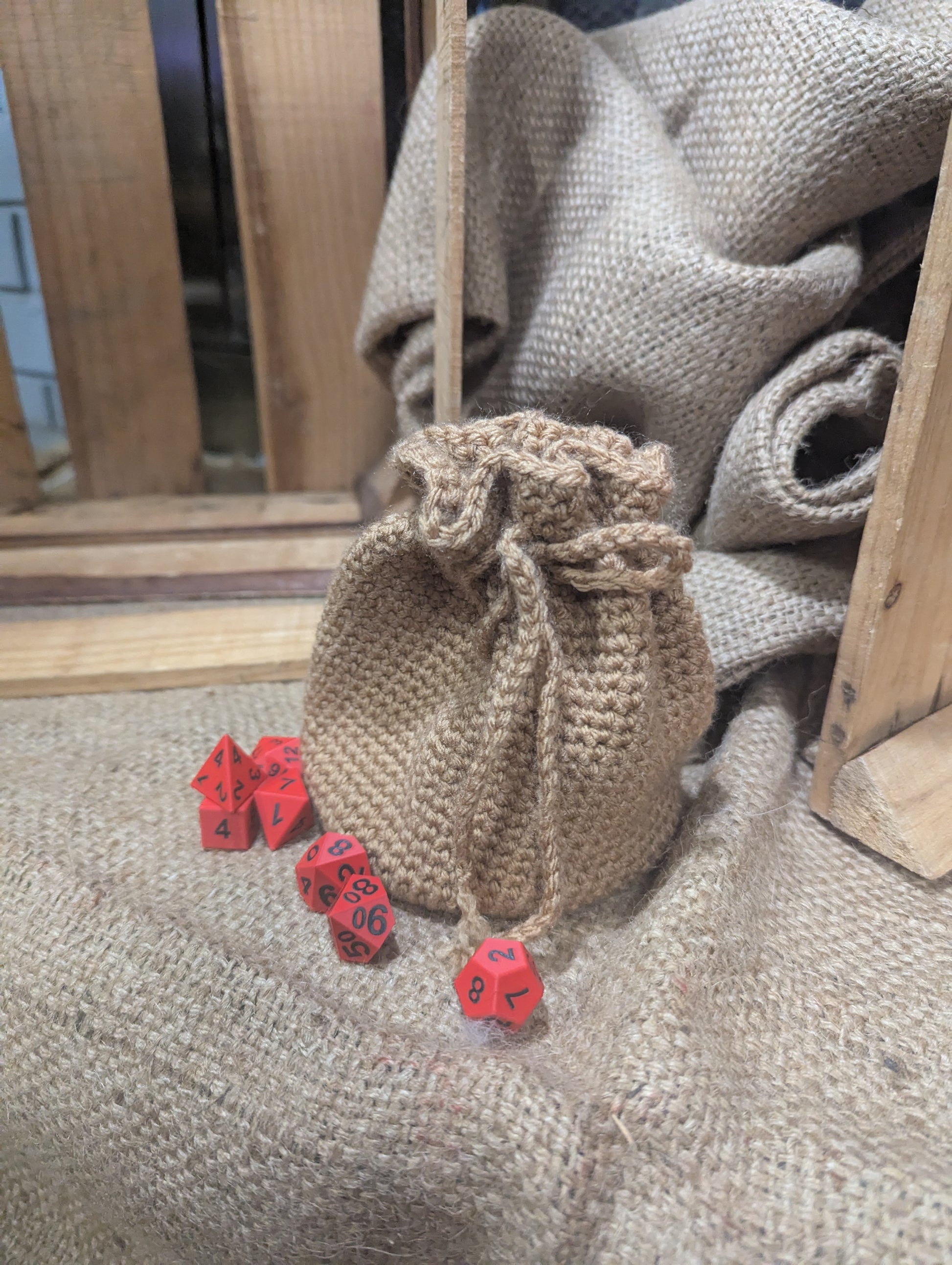 burlap crochet drawstring bag with red dice on a textured surface