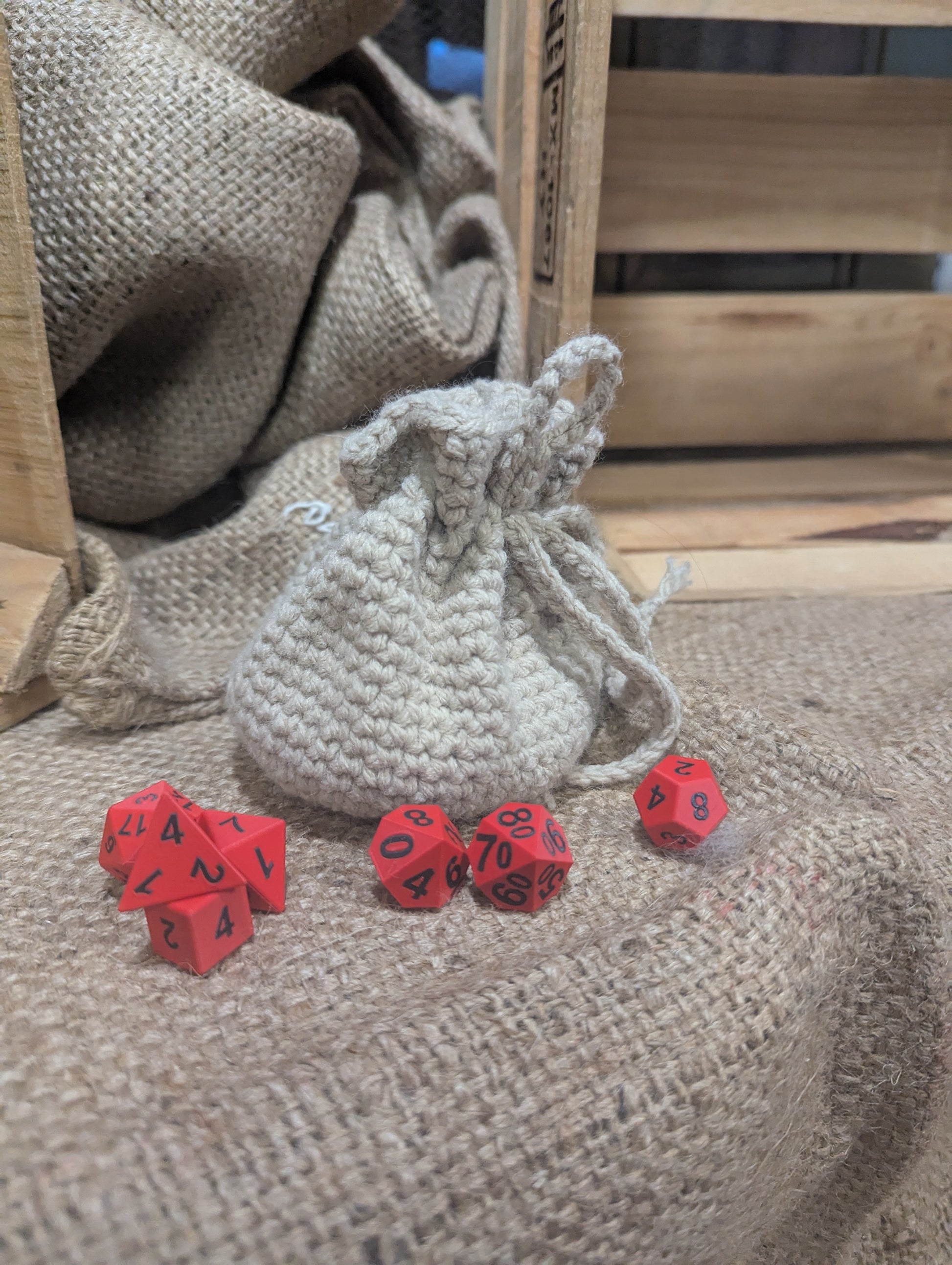 Red dice with black numbers on a textured surface next to a cream drawstring bag.