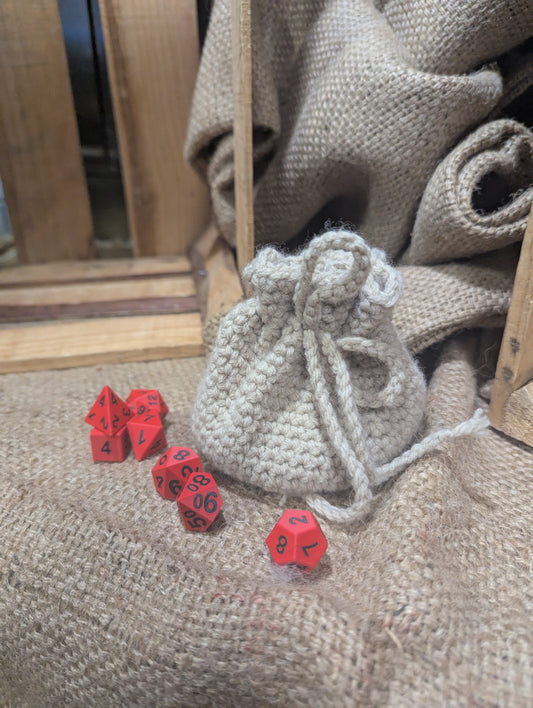 Red dice with black numbers on a textured surface next to a cream colored  drawstring bag.